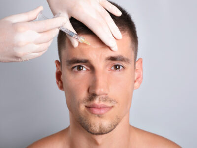 Man getting facial injection on grey background, closeup. Cosmetic surgery